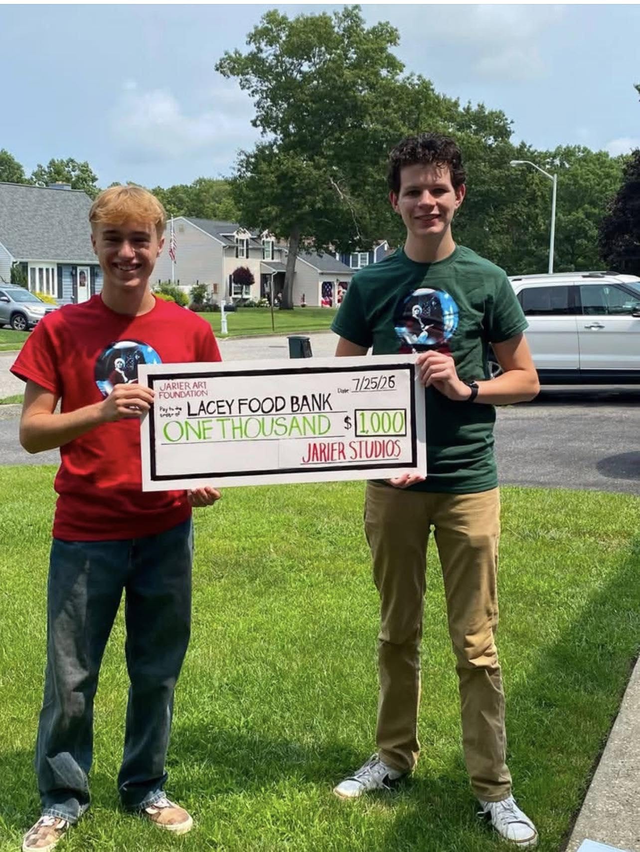 Two students of high school or college age presenting an oversized check to the Lacey Food Bank for $1000