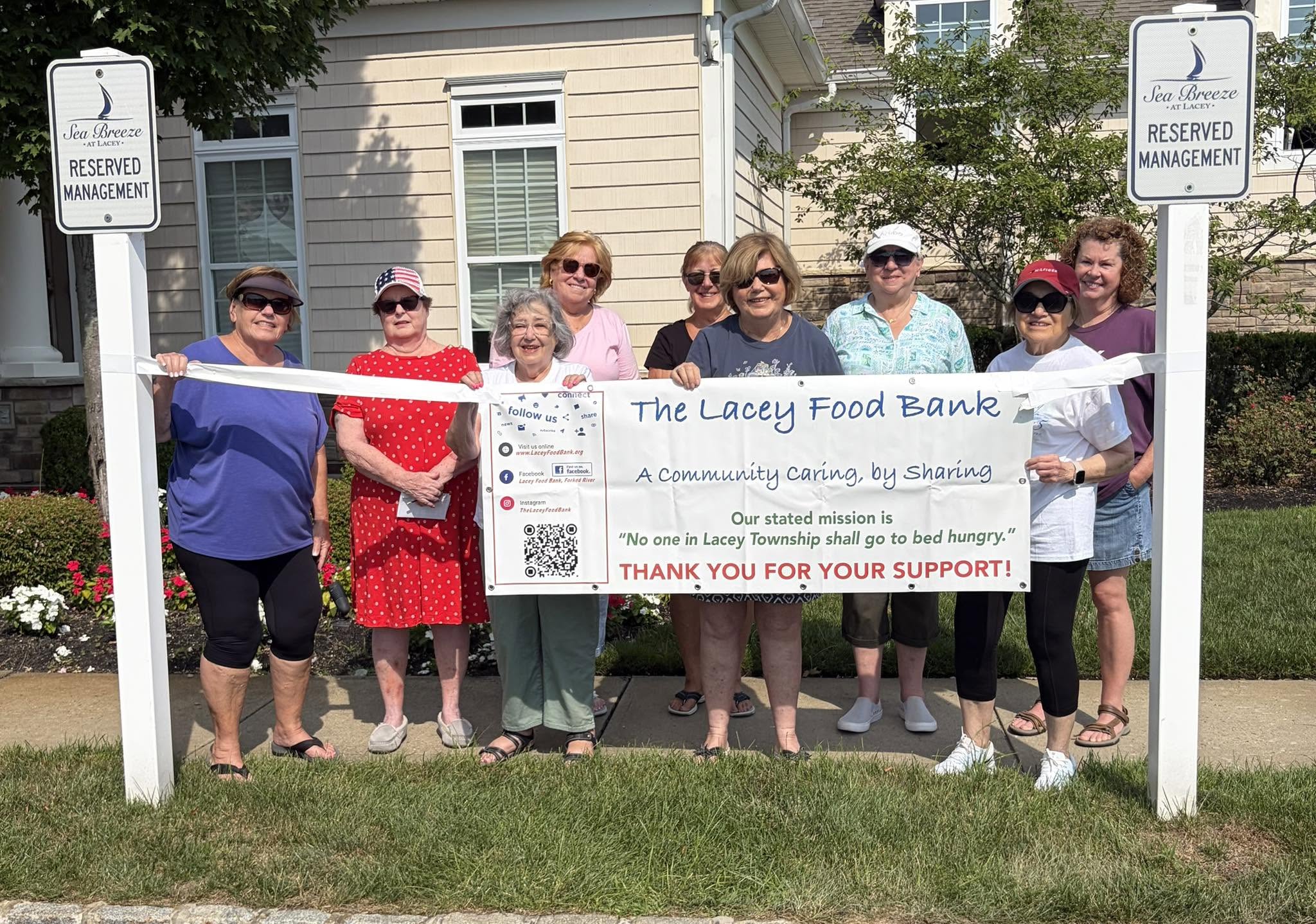 Group of people from Sea Breeze adult community standing behind a Lacey Food Bank Banner.