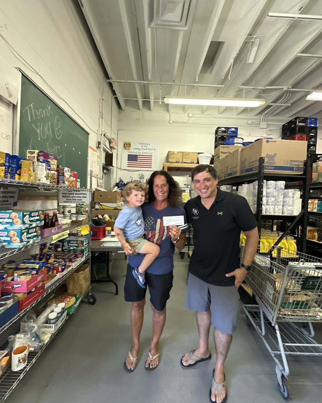 Man and women standing in the lacey food bank. Woman is holding a child. woman is also holding a check that was given to her for a donation to the food bank.